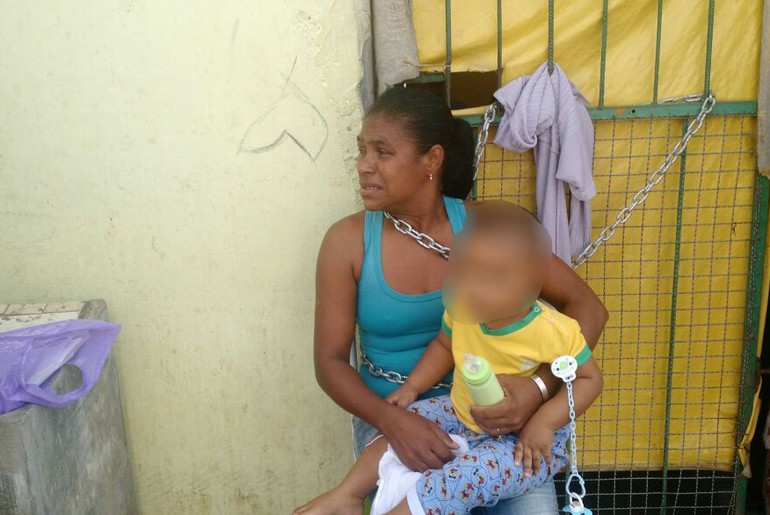 Mulher se acorrenta na porta de casa com bebê no colo